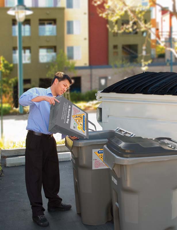 A young man empties his recycling bag into a recycling bin at his apartment complex