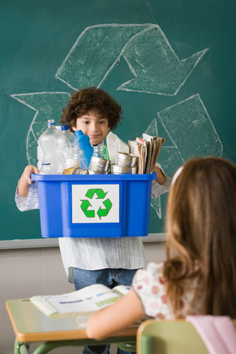 Student at front of classroom holding a recycling bin full of recyclable items for the class to see
