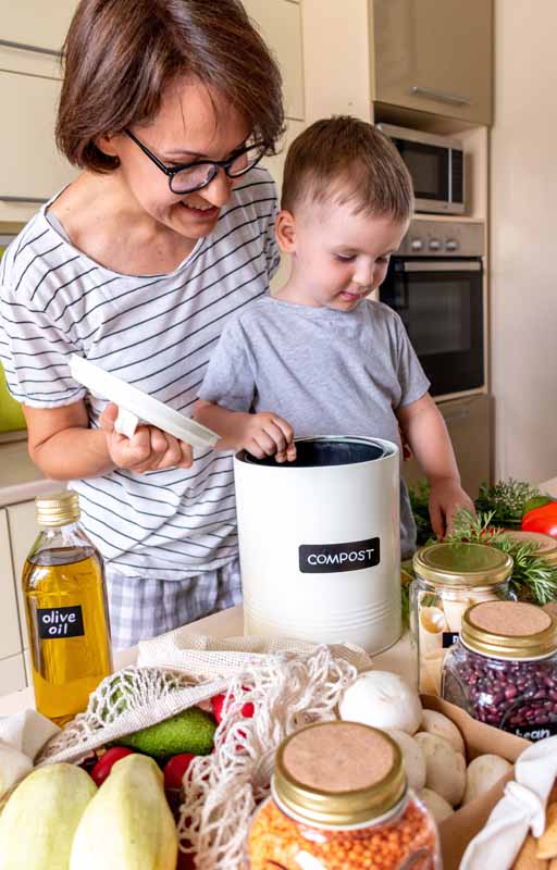Boy and mom at home in kitchen preparing a meal put food waste into the compost bin