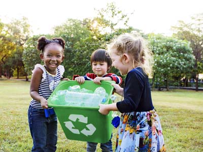 Group of elementary school children smiling while carrying a green recycle bin with plastic bottles