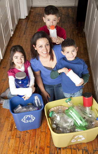 Mom sitting on floor with her three children sorting out recyclable items into different bins