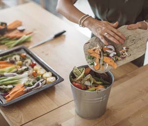 Women preparing vegetables for a meal places leftovers from cutting board into a composting pail