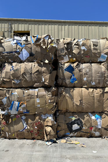 Bundles of crushed cardboard boxes outside a warehouse door at a recycling center